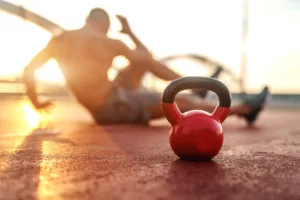 Silhouette of shirtless man doing crunches in the court in the morning. Selective focus on kettlebell.